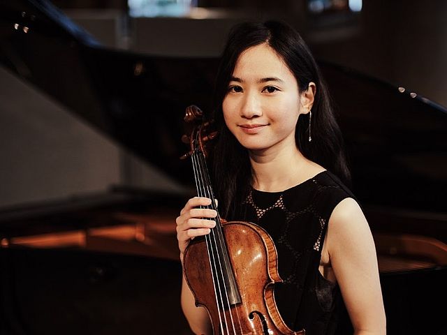 Junge, japanische Frau sitzt mit ihrer Geige vor einem Flügel. 