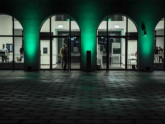 Haupteingang der Hochschule wird von grünen Strahlern angeleuchtet.