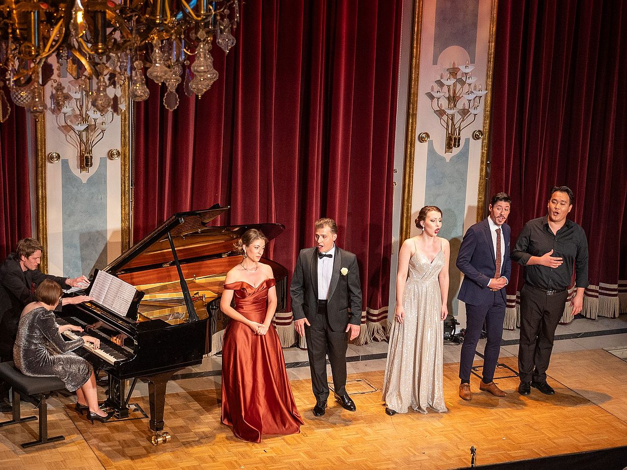 Zwei Sängerinnen und 3 Sänger stehen auf der Bühne im prunkvollen Glucksaal. Neben ihnen steht der Flügel, an dem die Pianistin Urszula Barnaś sitzt. 