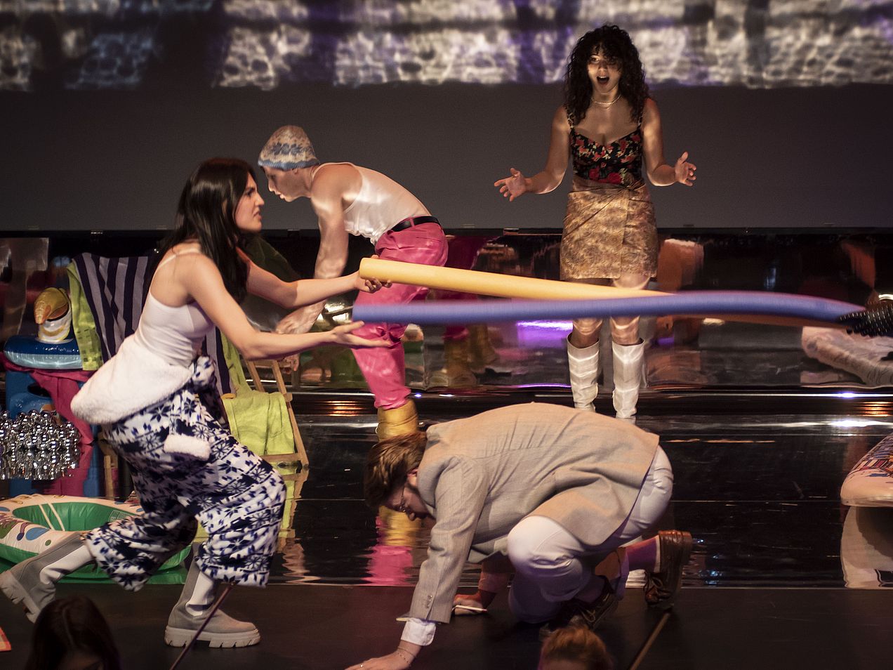 Im Vordergrund befindet sich eine Frau, die zwei Schwimmnudeln hält. Unter diesen hockt ein Mann mit Blick auf dem Boden. Im Hintergrund befinden sich eine Sängerin, die frontal zum Publikum steht und singt, während neben ihr ein Mann einen Liegestuhl nach vorne zieht. 