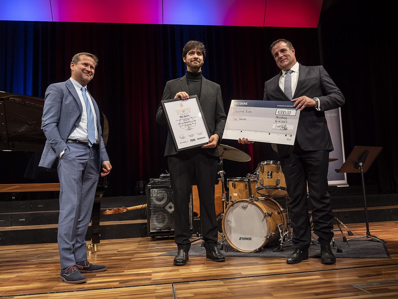 Magi García steht in der Mitte zwischen Thomas Biller (BW Bank) und Michael Wiesengrund (Piano Haid). Er hält die Steinway-Urkunde und Thomas Biller den 1000€-Scheck in den Händen.