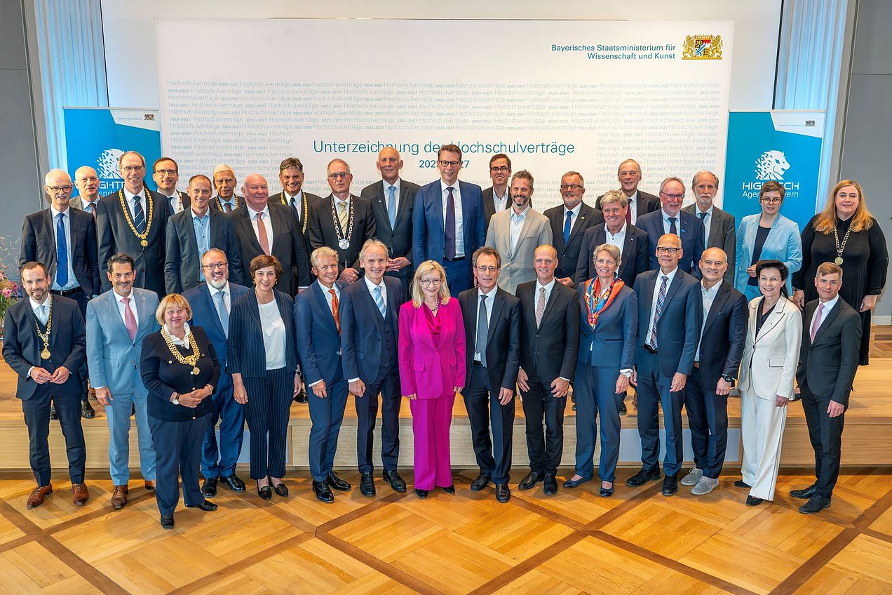 Gruppenbild von Markus Blume mit den 33 unterzeichnenden Hochschulleitungen vor einer Pressewand mit der Aufschrift "Unterzeichnung der Hochschulverträge 2023-2027". 