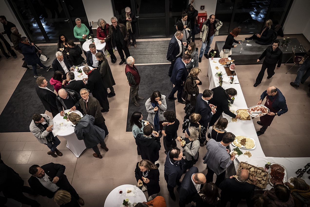 Aufnahme von der Galerie mit Blick auf das Foyer. Ca. 40 Personen stehen an Stehtischen bzw. am Buffet . 