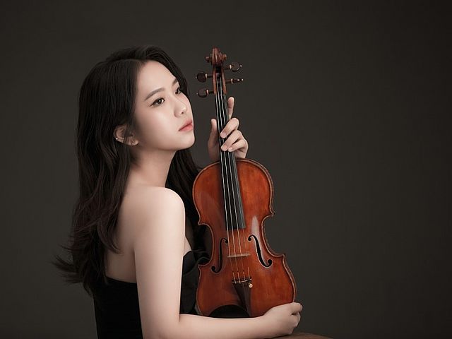 Porträt einer jungen, koreanischen Frau im Profil. Sie schaut nach rechts und hält ihre Geige auf der rechten Seite.