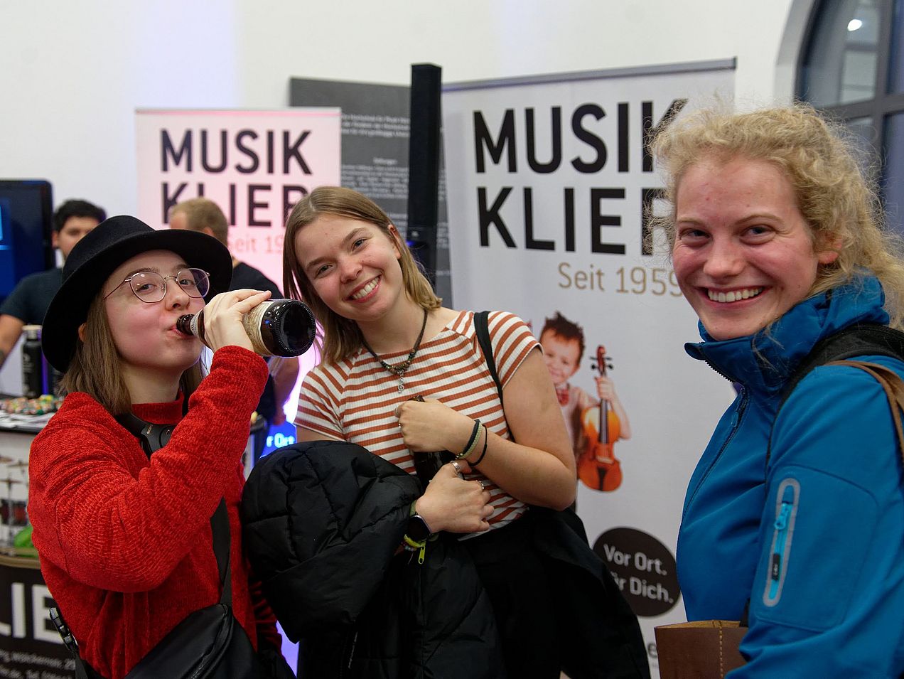 Drei Studentinnen stehen nebeneinander im Foyer und lächeln in die Kamera. 