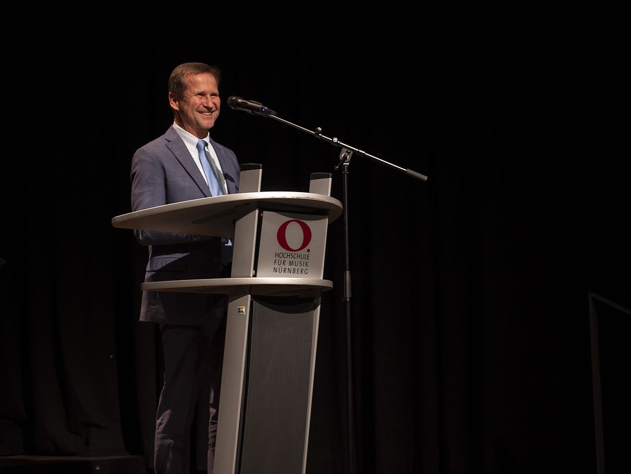 Michael Wiesengrund steht am Rednerpult auf der Bühne des Orchestersaals. 