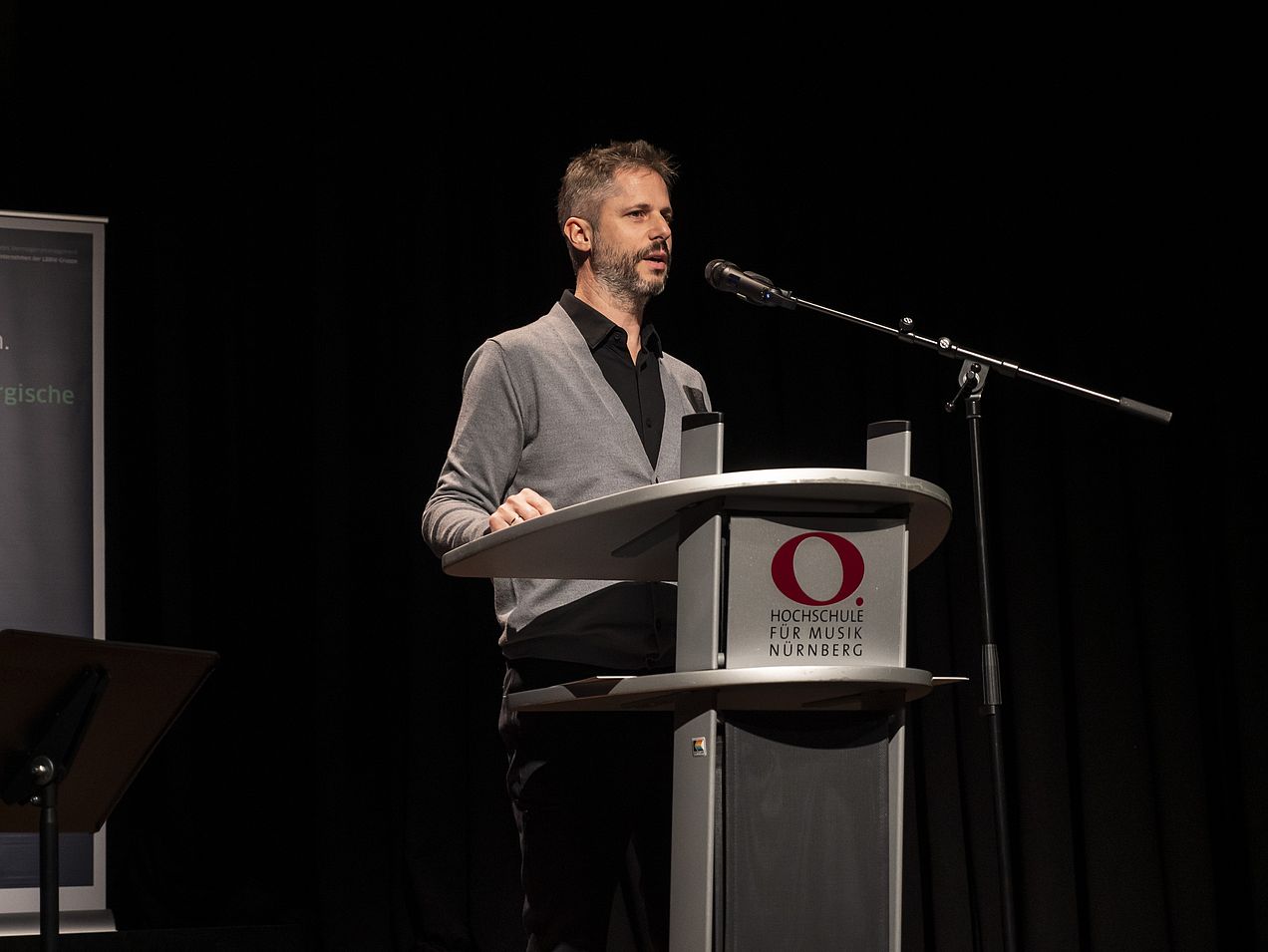 Präsident Prof. Rainer Kotzian steht am Rednerpult auf der Bühne des Orchestersaals. 