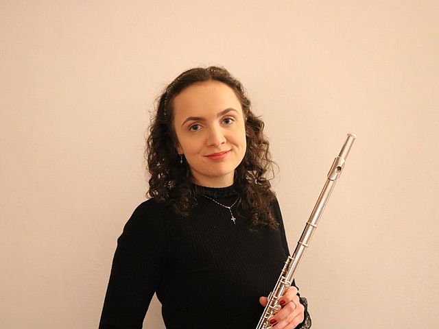 Porträt der jungen Frau mit dunklen, langen Locken. In den Händen hält sie ihre Querflöte.