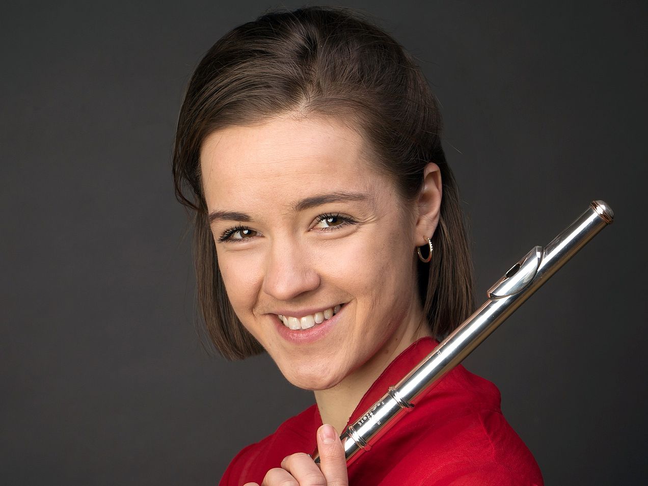 Porträt Emma Hochschild. Die junge Frau mit kurzen, dunklen Haaren hält ihre Querflöte über ihre Schulter. 