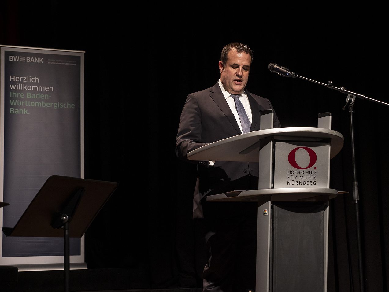 Thomas Biller steht am Rednerpult auf der Bühne des Orchestersaals. 