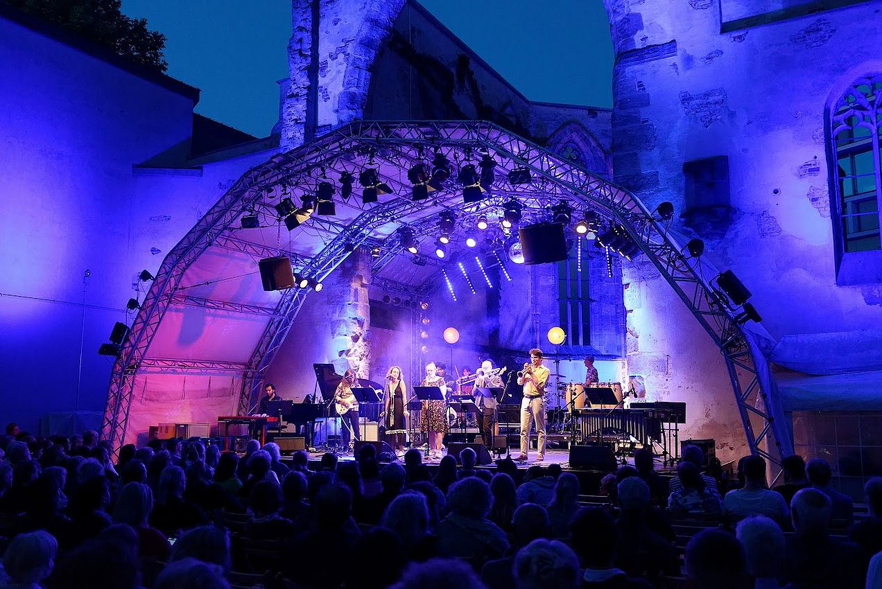 Erleuchtete Bühne vor der Katharinenruine. Mitglieder der Big Band stehen auf der Bühne und spielen Klavier, Trompete, Posaune, Schlagzeug und Bass bzw. singen. 