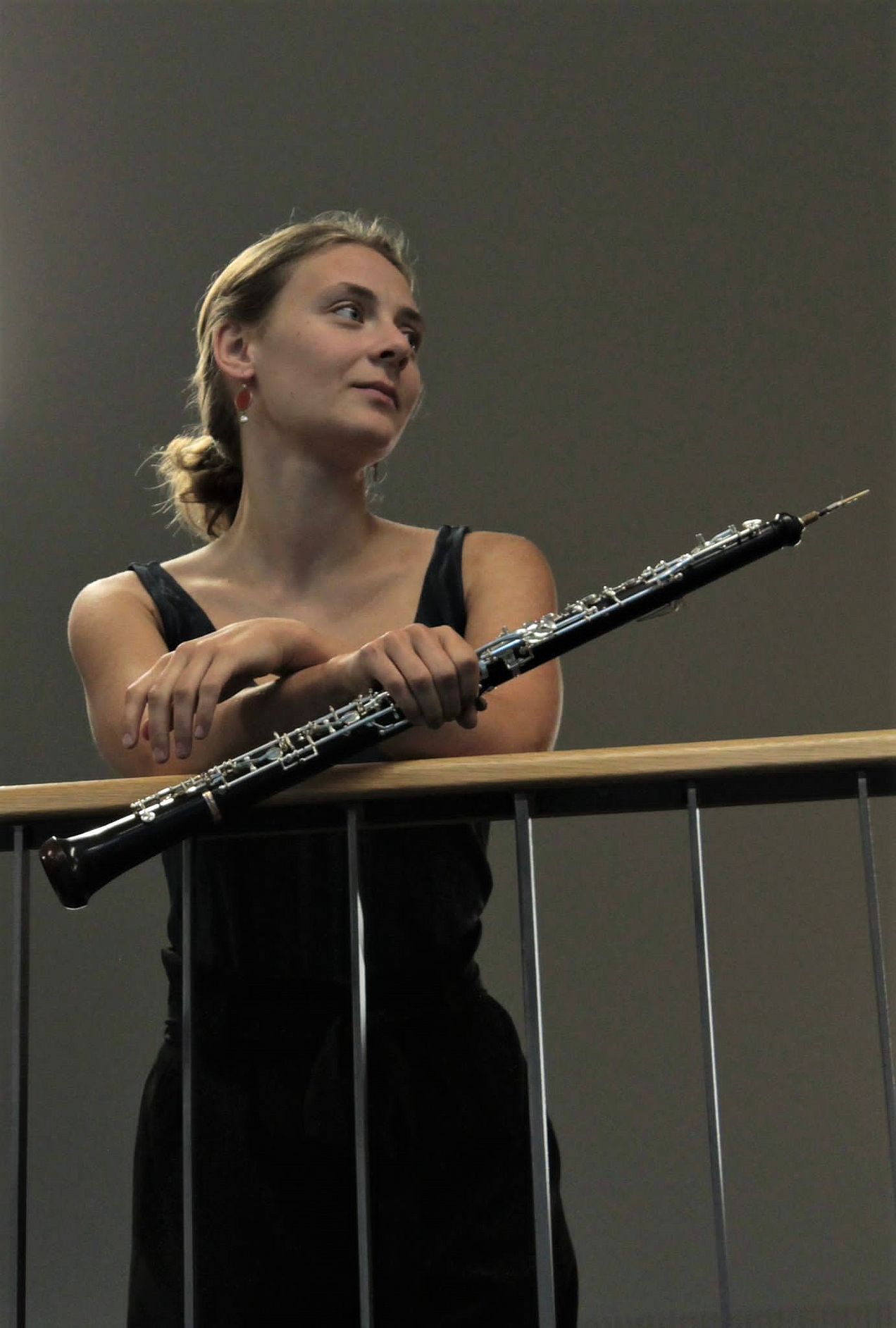 Porträt von Magdalena Steinbauer, die ihre Arme über ein Geländer legt und mit der rechten Hand ihre Oboe hält. Sie schaut freundlich lächelnd zur Seite. 