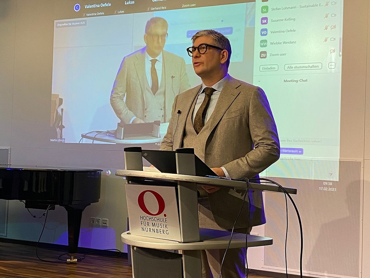 Jacobus Bracker steht am Rednerpult, an die Wand hinter ihm wird die Übertragung in der Zoom-Konferenz projiziert. 