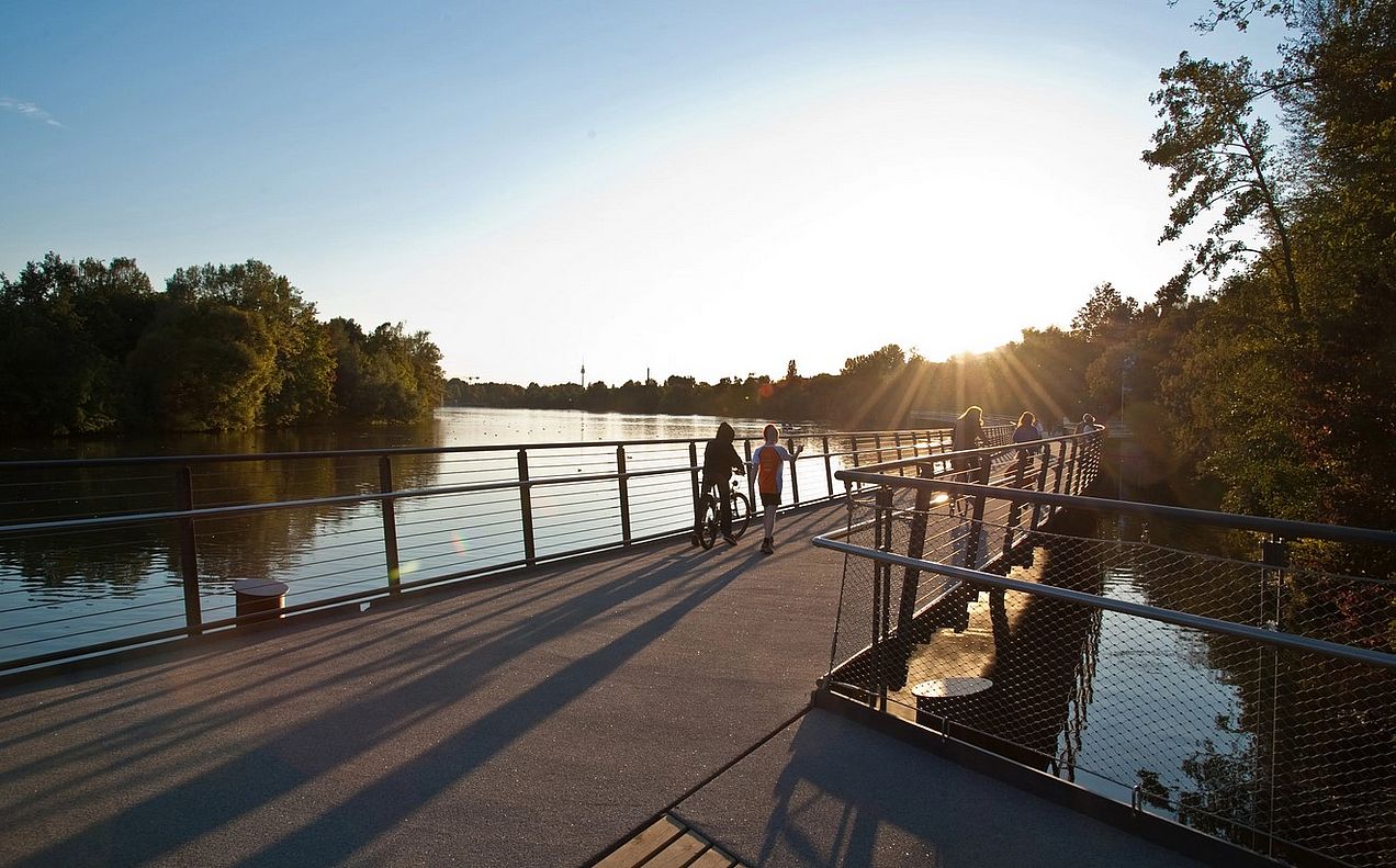 Ein Steg führt durch den Wöhrder See, im Hintergrund ein Sonnenuntergang