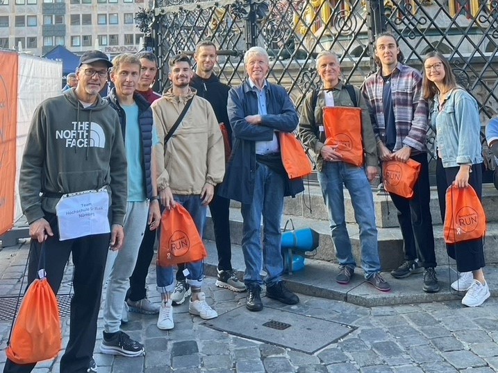 Gruppenfoto der Teilnehmer*innen der Hochschule beim Stadtlauf. Die Teilnehmer*innen halten orangene Sportbeutel in den Händen. 