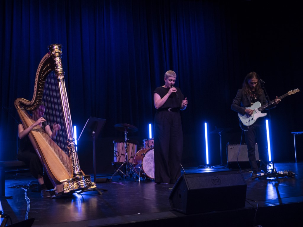 Lauren Schrempp sitzt links im Bild, Harfe spielend. Daneben steht Ottilie Niebauer, Gesang. Auf der rechten Seite steht Andreas Werner und spielt Gitarre. 